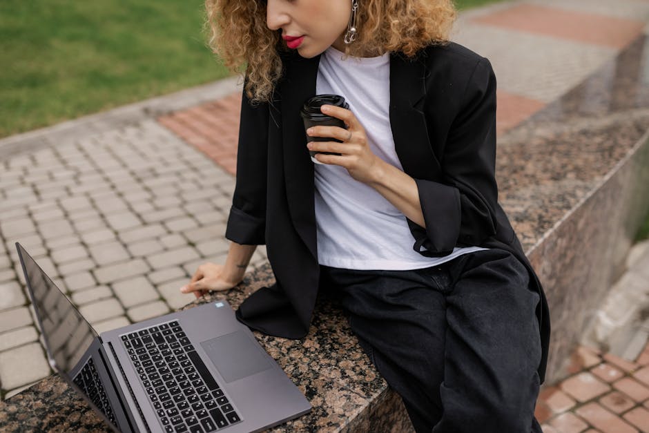 Professional woman sitting outdoors with coffee and laptop, engaged in remote work.