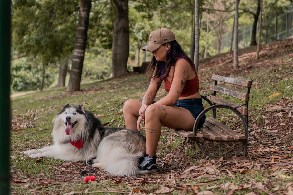 Woman sitting with Alaskan Malamute in a tranquil park setting, enjoying a peaceful moment outdoors.